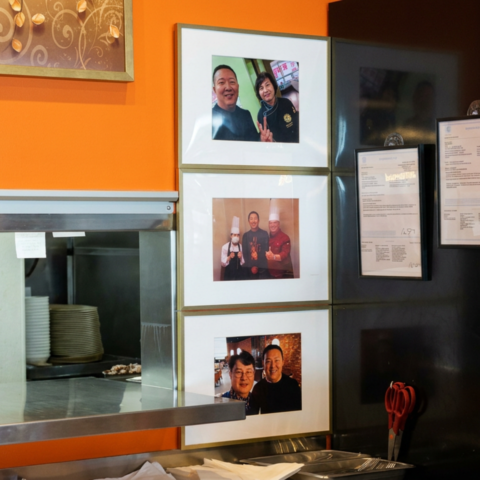 Restaurant interior showing an open kitchen counter, framed staff and customer photographs, posted menus, and a beverage refrigerator.